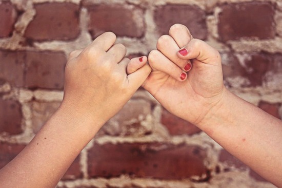 Two kids make a pinky promise (by linking their pinky fingers)